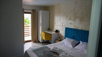 A hotel room with a bed, a desk, a chair, and a view of the outdoors through a door.