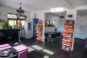 A room with a bar area, a refrigerator, a vending machine, and a snack display.
