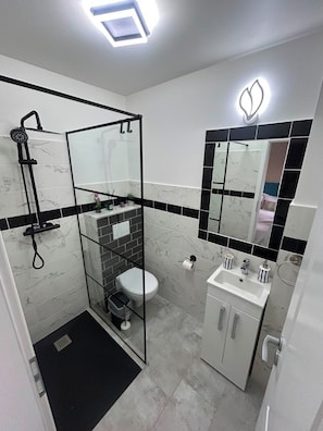 Un baño moderno con ducha de vidrio, inodoro, lavamanos y espejo con luz decorativa.