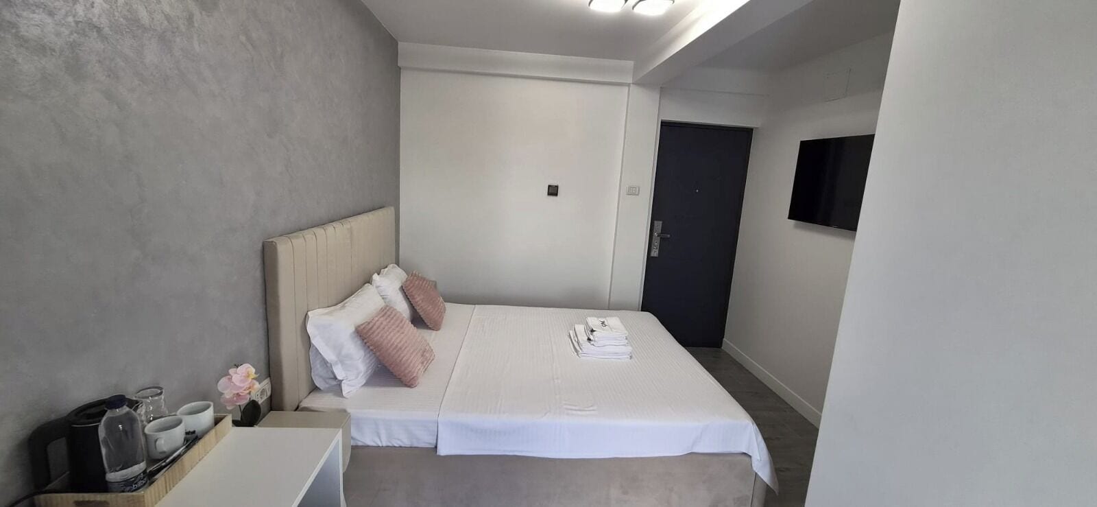 A hotel room with a bed, bedside table, and a television mounted on the wall.