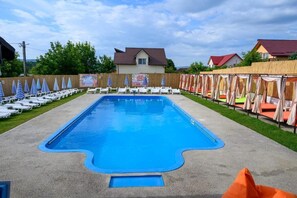 A swimming pool with lounge chairs and umbrellas, surrounded by a wooden fence and houses.