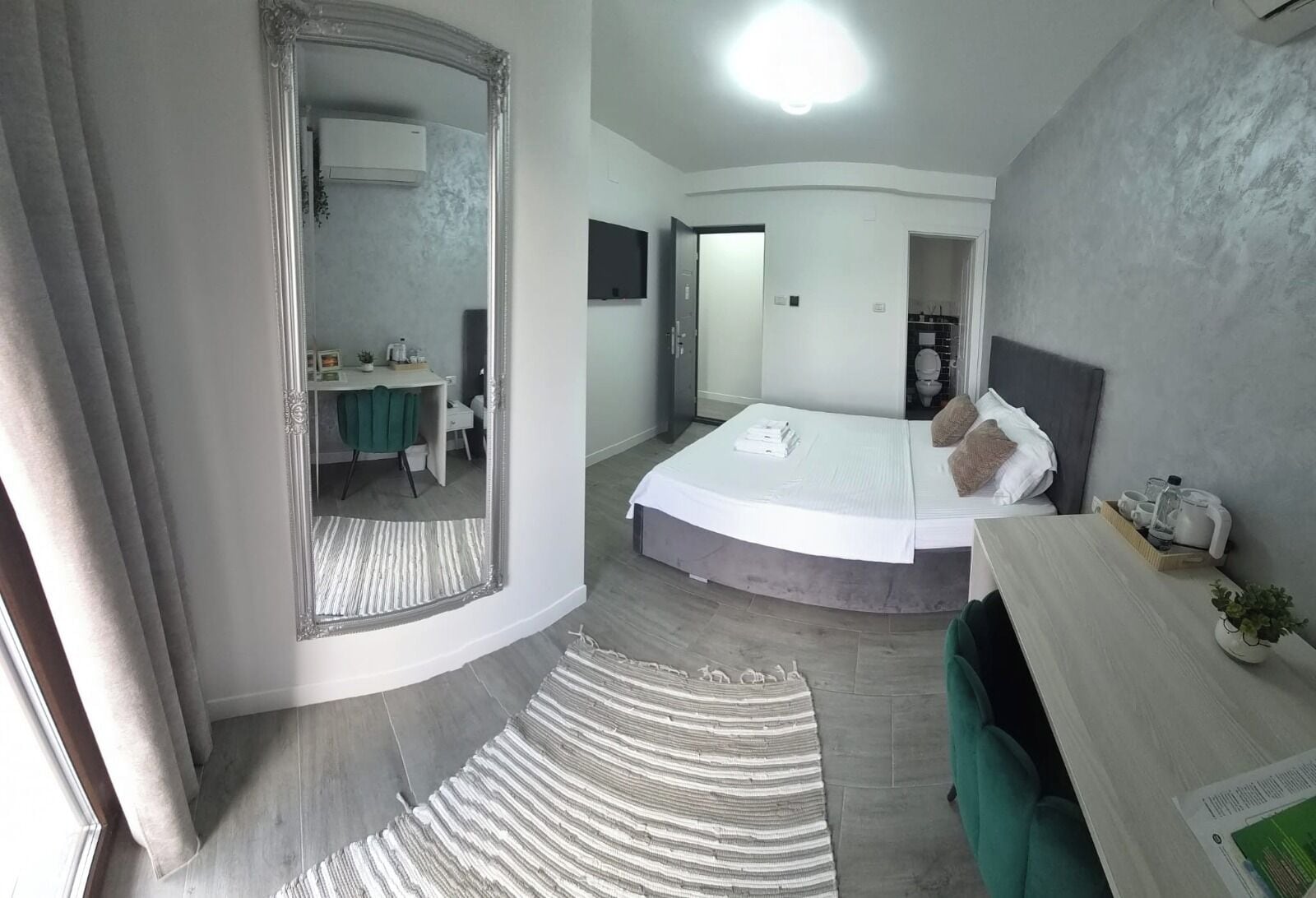 A modern bedroom with a curved bed, a bedside table, a mirror, and a view into the bathroom.