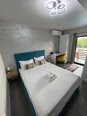 A modern bedroom with a large bed, a bedside table, a nightstand, a wardrobe, and a bathroom with a mirror and sink. - Good Mood Pool & Smart Rooms (Ciurea)