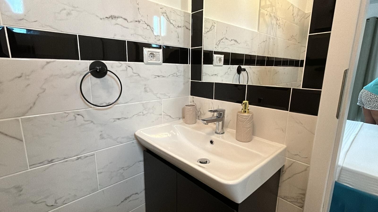 A bathroom with a white sink, black and white tiled walls, a mirror, and a towel ring.