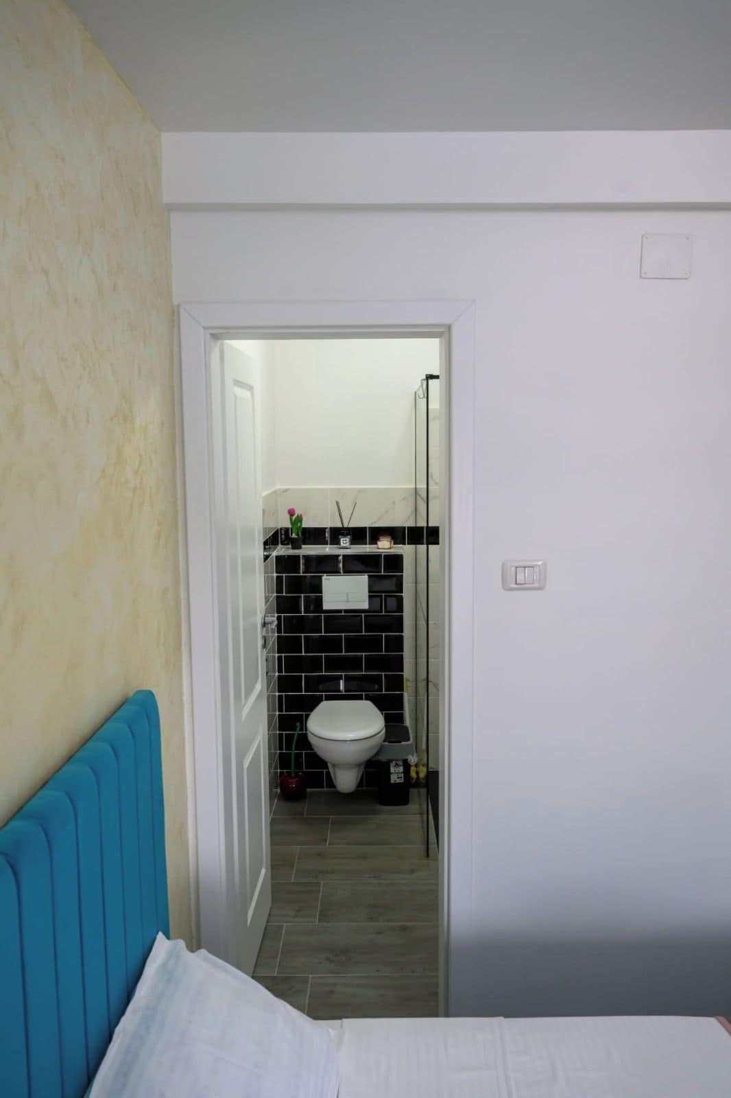 A bedroom with a bed, a bathroom with a toilet and a sink, and a door leading to another room.