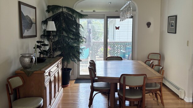 A dining area with a wooden table and chairs, a potted plant, and a view through a glass door. -  Beautiful Light-Filled Home In Charming Historic Cold Spring (Cold Spring)