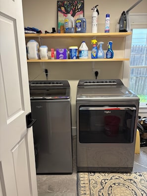 A compact kitchen with two stainless steel appliances, a shelf with cleaning products, and a window with a view.