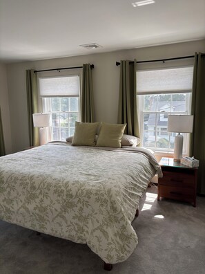 A bedroom with a large bed, two bedside lamps, a nightstand, and a view through the window.