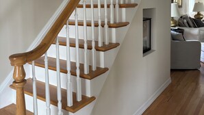 A staircase with wooden steps and white balusters, leading to a living area with a sofa and a fireplace. -  Beautiful Light-Filled Home In Charming Historic Cold Spring (Cold Spring)