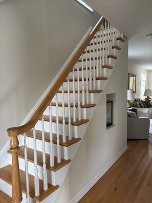 Eine Treppe mit Holzstufen und weißen Geländern, die zu einem Wohnbereich mit Sofa und Kamin führt.