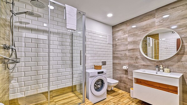 A modern bathroom with a glass shower enclosure, a washing machine, and a vanity with a mirror. - Apartamenty Sun & Snow Sowa (Szklarska Poręba)