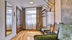 Ein Flur mit Holzboden, einem grünen Sofa, einem Sessel, einem Kleiderhaken und einer Tür mit Spiegel.