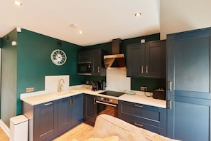A compact kitchen with dark cabinetry, a built-in oven, and a coffee machine. - Chic 1BR Flat with Parking-Easy access to City Center (Leeds)