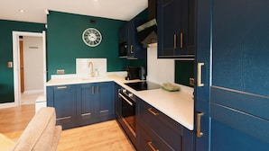 Een moderne keuken met donkere kastjes, een wit aanrechtblad en een hangend horloge.