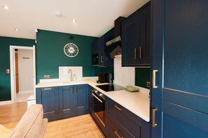 A modern kitchen with dark cabinetry, a white countertop, and a wall-mounted clock. - Chic 1BR Flat with Parking-Easy access to City Center (Leeds)