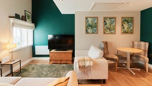 Een woonkamer met een televisie, een open haard, een bank, een fauteuil en een kleine tafel.