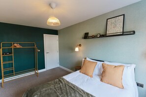 A hotel room with a bed, a wardrobe, a shelf with decorative items, a wall clock, and a hanging light fixture. - Chic 1BR Flat with Parking-Easy access to City Center (Leeds)