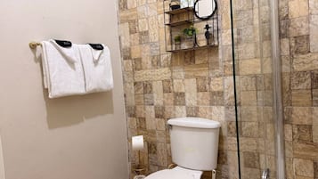 Un baño con inodoro, cabina de ducha de vidrio y toallero con dos toallas blancas.