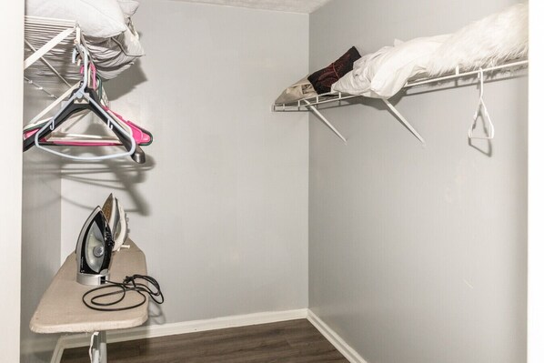 A small, neatly organized closet with hanging space and an ironing board.