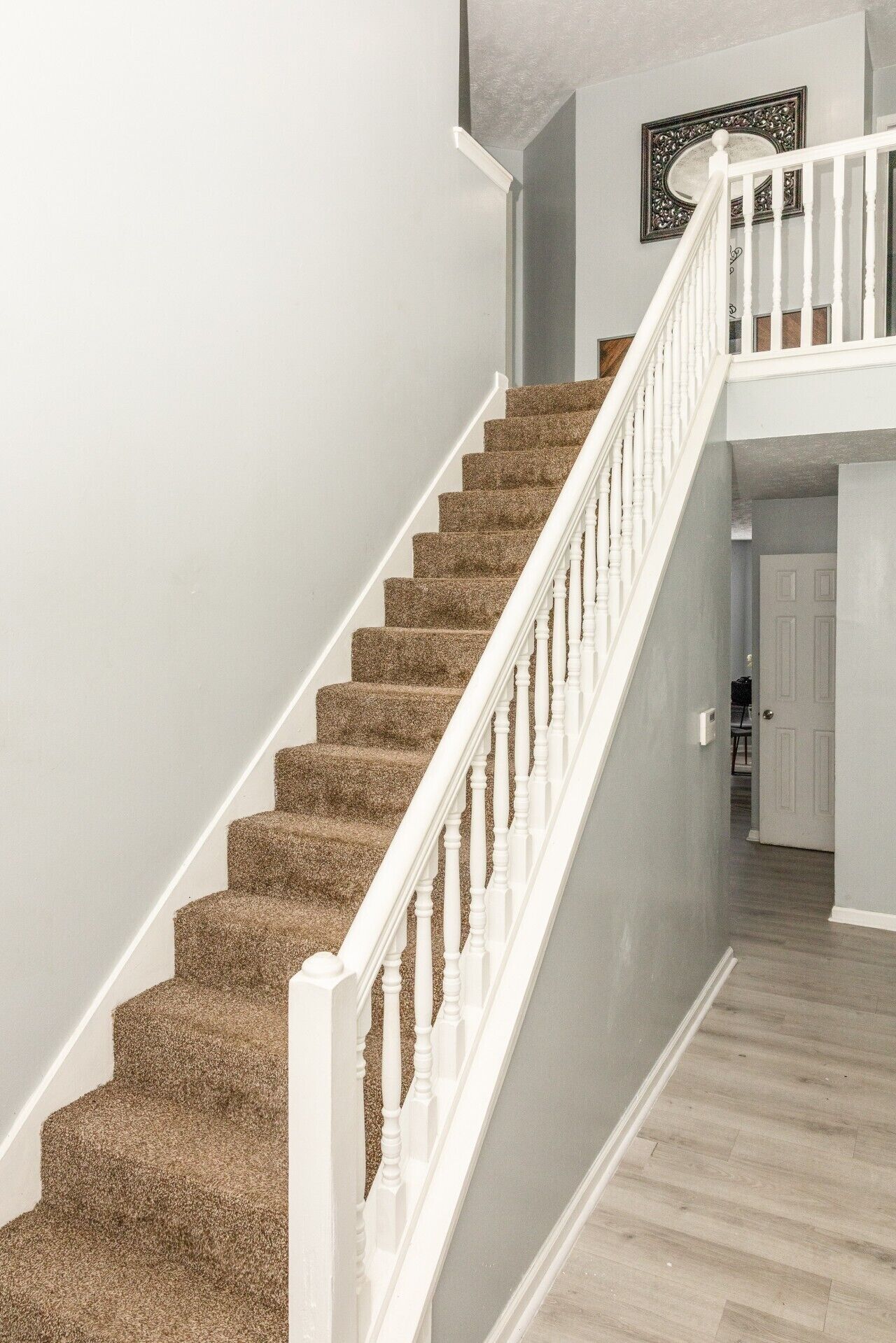 A staircase with carpeted steps and white balusters, leading to a landing with a door.