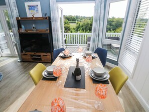 A dining area with a table set for four, a television, and a view of the outdoors. - Pleasant Valley Holiday Lodge 70 (Narberth)