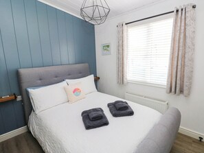 A bedroom with a bed, pillows, a bedside table, a window with curtains, and a radiator. - Pleasant Valley Holiday Lodge 70 (Narberth)