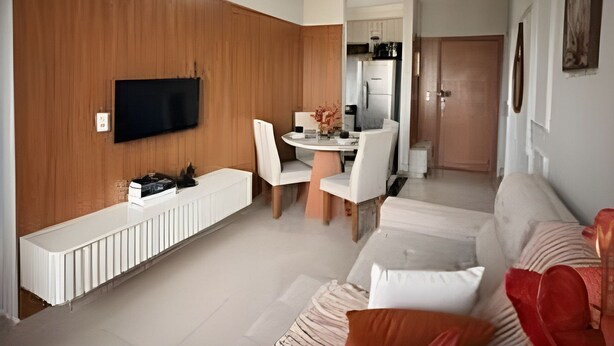 Een moderne woonkamer met een flatscreen televisie, een eethoek met een tafel en stoelen, en een keuken op de achtergrond.