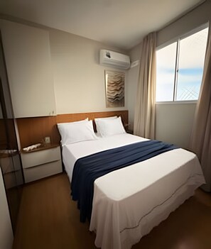 A hotel room with a bed, a nightstand, a window with curtains, and an air conditioning unit on the wall. - Apto I Piscina I Wi-Fi I Conforto- Lazer (Cabedelo)