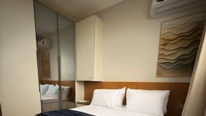 Een hotelkamer met een bed, een spiegel, een wandairconditioner en een schilderij.