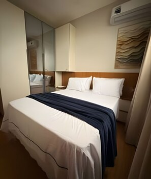 Ein Hotelzimmer mit einem Bett, einem Spiegel, einer Wand-Klimaanlage und einem Gemälde.