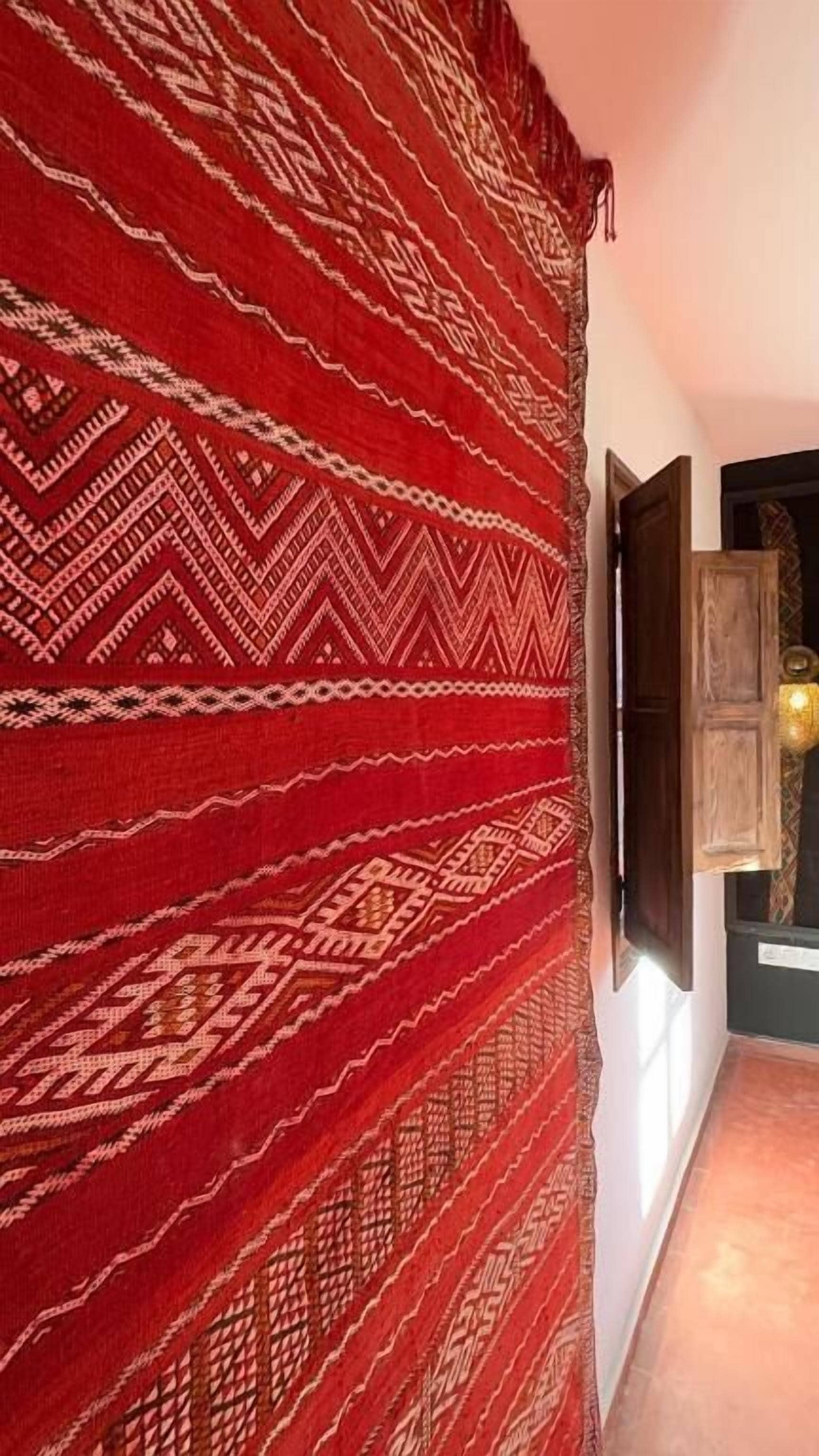A hallway with a patterned red carpet, a wooden door, and a wall-mounted television.
