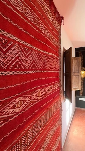 A hallway with a patterned red carpet, a wooden door, and a wall-mounted television. - RIAD TILÉLI (Marrakech)
