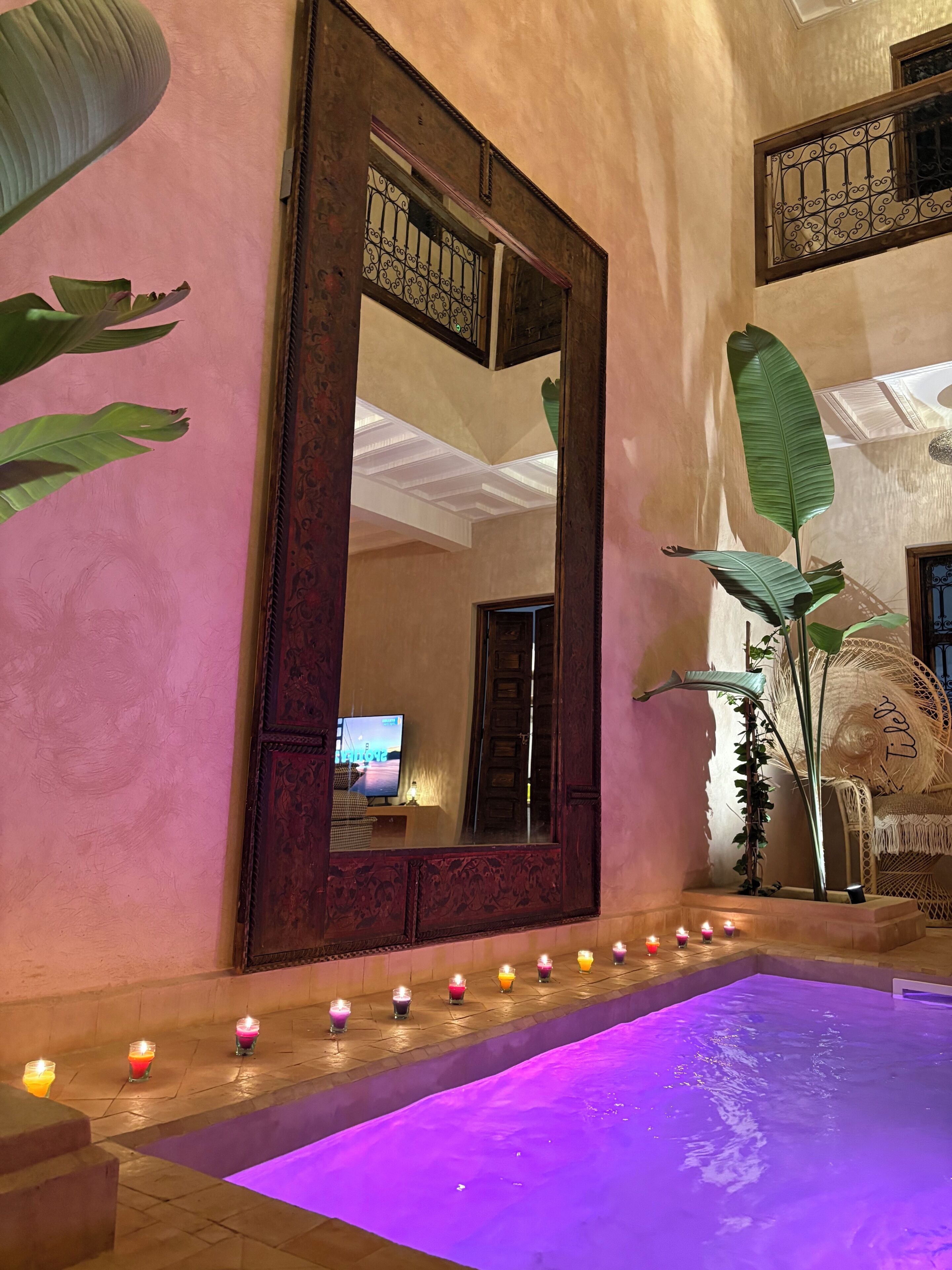 Una habitación con un espejo grande, una piscina con iluminación púrpura y velas a lo largo de la piscina.
