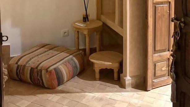 Ein Zimmer mit einer Holztür, einem kleinen Hocker, einem Kissen und einem Wandbild.