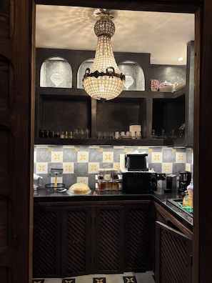 Una cocina con candelabro, repisas con cristalería, cafetera y salpicadero decorativo.