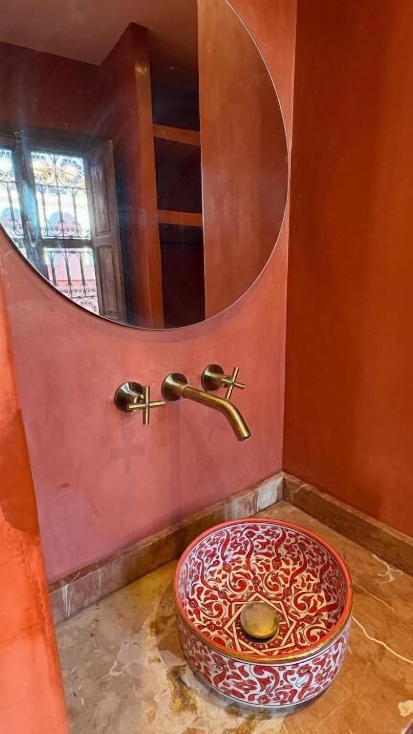 A bathroom with a round mirror, a brass faucet, and a patterned basin.