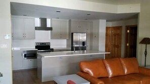 Et moderne køkken med rustfrie stålgrej, en central ø og en lædersofa i en opholdsstue.