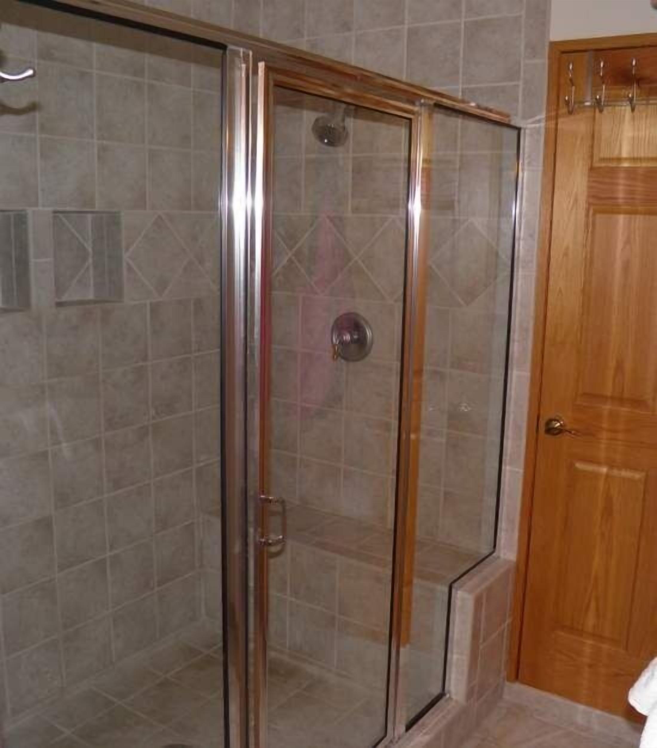 A shower enclosure with a glass door and a wooden door adjacent to it.