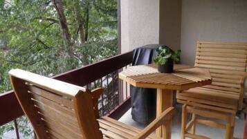 Un balcón de madera con una mesa, sillas, una planta en maceta y vista a árboles.