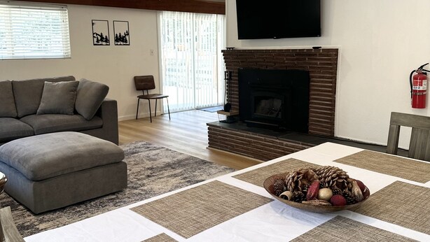 A living room with a fireplace, a sofa, a television, and a dining area with a table set for two. - Hch0681 - Red Lake Lodge 3 Bedroom Home (South Lake Tahoe)