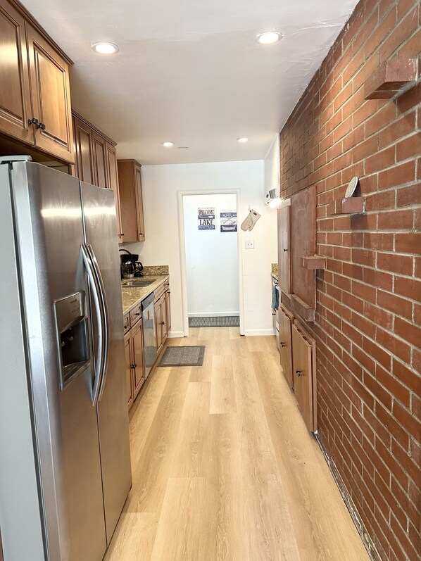 A kitchen with a stainless steel refrigerator, wooden cabinets, a brick wall, and a welcome sign. - Hch0681 - Red Lake Lodge 3 Bedroom Home (South Lake Tahoe)