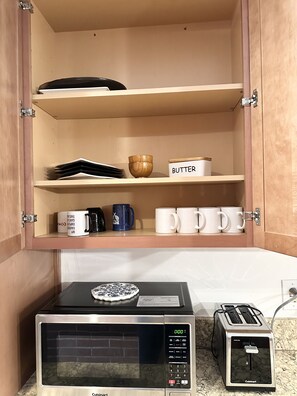 Eine Küche mit Mikrowelle, Toaster und einem Schrank mit Tassen und einer Kaffeemaschine.