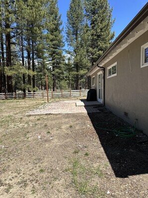 A building with a paved patio area, surrounded by a wooden fence and tall pine trees. - Hch0681 - Red Lake Lodge 3 Bedroom Home (South Lake Tahoe)