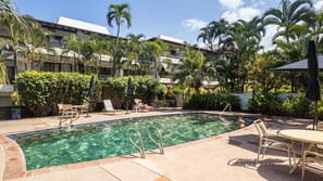 Ein Swimmingpool mit Liegestühlen und Sonnenschirmen, umgeben von Palmen und einem Gebäude mit Balkonen.