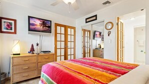 A bedroom with a bed, a television, a dresser, and a door leading to another room. - Big Island Casa De Emdeko B326 1 Bedroom Apts (Kailua-Kona)