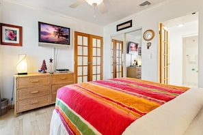 A bedroom with a bed, a television, a dresser, and a door leading to another room. - Big Island Casa De Emdeko B326 1 Bedroom Apts (Kailua-Kona)