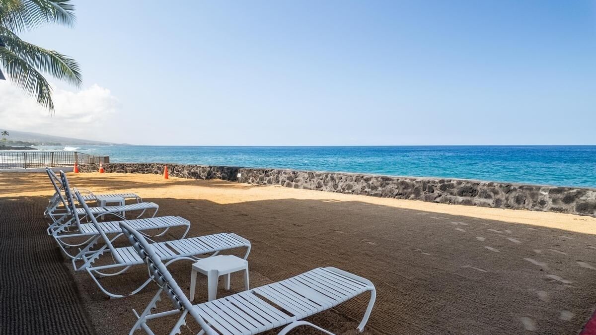 A beach with white lounge chairs and a stone wall.
