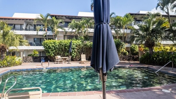 A swimming pool with a clear blue water surface, surrounded by a poolside area with lounge chairs and umbrellas. - Big Island Casa De Emdeko B326 1 Bedroom Apts (Kailua-Kona)