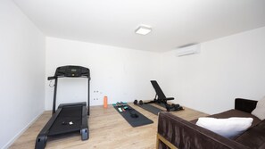 Ein kleines Zimmer mit Laufband, Fitnessgeräten und einem Bett.