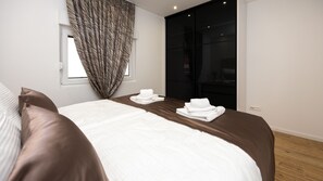 Ein modernes Hotelzimmer mit einem großen Bett, einem Fenster mit Vorhängen und einer dunklen Schiebetür.